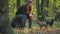 Woman with red hair sitting in a forest on a stump and caresses two little dogs