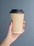 Woman with red manicure holds disposable brown paper cup coffee to go. Vertical mockup with copy space