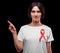 A woman with red ribbon pointing at something on a black background. Support people with AIDS. Health awareness concept.
