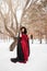 woman in a red rococo dress and a raincoat with a fur hood is walking with a lantern in her hands