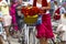 A woman in a red skirt holds the handlebars of a bicycle. Basket with poppies flowers. Frame part