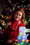 Woman in red sweater sits on a background of the Christmas tree with lights and decorated railing and smile