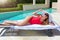 Woman in red swimsuit and white sunhat relaxes by the pool