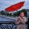 A woman with a red umbrella stands on a bridge in a strong wind