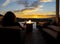 A woman relaxes with a glass of wine at night in front of an outdoor firepit on a patio of a luxury home overlooking a city.