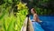 Woman relaxes in infinity pool at tropical villa. Red-haired lady tranquil water, rich plants. Serene escape luxury