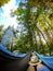 Woman relaxing in the hammock by the lake in the forest, POV view of legs in trekking boots with straw hat. Wanderlust concept
