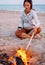 Woman relaxing near a campfire on beach.