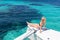 Woman relaxing on a summer sailing cruise, sitting on a luxury catamaran near picture perfect white sandy beach on