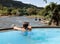 Woman relaxing in swimming pool and watching a Herd of Young elephants in river water hosing in Pinnawala Elephant Orphanage