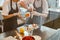 Woman removes cream leftovers from bun near colleague with confectioner bag at metal table