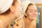 Woman removing facial clay mud mask in bathroom