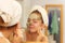 Woman removing facial clay mud mask in bathroom