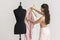 Woman removing pink jacket from tailors dummy to place on hanger.