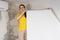 A woman repairman glues white wallpaper on the wall near the air conditioner under the ceiling.