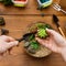 Woman replanting succulent plants in glass florarium vase on wooden table.