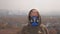 A woman in a respirator stands on the background of smoking factory pipes