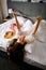 Woman resting in bed with tasty set of sushi rolls, fashion magazine and flowers bouquet