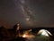 Woman resting at night camping near campfire, tourist tent, bicycle under evening sky full of stars