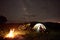 Woman resting at night camping near campfire, tourist tent, bicycle under evening sky full of stars