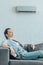 woman resting on sofa with air conditioner on wall summer