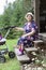 A woman of retirement age sits on the porch of a wooden house and shakes a pram with a baby