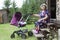 A woman of retirement age walks with a children pram in the yard of a summer cottage, near the wooden house