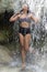 Woman in a retro swimsuit showering under a waterfall