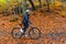 Woman riding bicycle in city forest in autumnal scenery