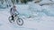 Woman is riding bicycle near the ice grotto. The rock with ice c