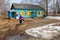 A woman is riding a bicycle to an old wooden rural mail building through a puddle.