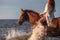 a woman riding a brown horse into the ocean waves of the shore