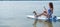 A woman is riding a sup surfboard with a dog on the lake. The girl goes in for water sports with her pet.