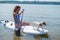 A woman is riding a sup surfboard with a dog on the lake. The girl goes in for water sports with her pet.