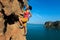 Woman rock climber climbing at seaside cliff