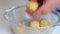 A woman rolls dough into balls to bake cakes. Nearby there are metal forms for baking cake, filled with dough and stuffing from a
