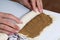 A woman rolls up the rolled dough with a layer of cinnamon into a tube. Cooking buns