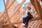 Woman roofer sitting on wooden beam of roof construction and talking phone