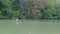 Woman rowing kayak on river on bank of which there are many green trees