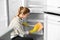 Woman in rubber gloves cleaning empty refrigerator with rag at home