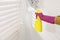 Woman in rubber gloves spraying mold remover onto wall in room, closeup