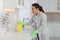 Woman in rubber gloves using mold remover on wall in kitchen