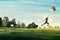 Woman running and jumping touch balloons floating in the sky on green grass and flower field