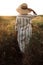 Woman in rustic dress and hat enjoying peaceful sunset in wildflowers and herbs in summer meadow. Atmospheric authentic moment.