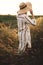 Woman in rustic dress and hat enjoying peaceful sunset in wildflowers and herbs in summer meadow. Atmospheric authentic moment.