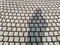Woman`s black shadow standing on grey cobblestone curve pattern paving on the street