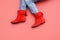 Woman`s Caucasian legs in blue jeans and red suede leather short angle boots without heels pink crimson colour background. Copy