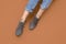 Woman`s Caucasian legs in blue twisted jeans and gray suede English brogue Oxfords shoes isolated on Brown beige background.