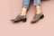Woman`s Caucasian legs in blue twisted jeans and gray suede English brogue Oxfords shoes  on light pink beige background.