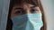 Woman`s face in protective medical blue mask, close up. Young female wearing medical mask for virus infection prevention